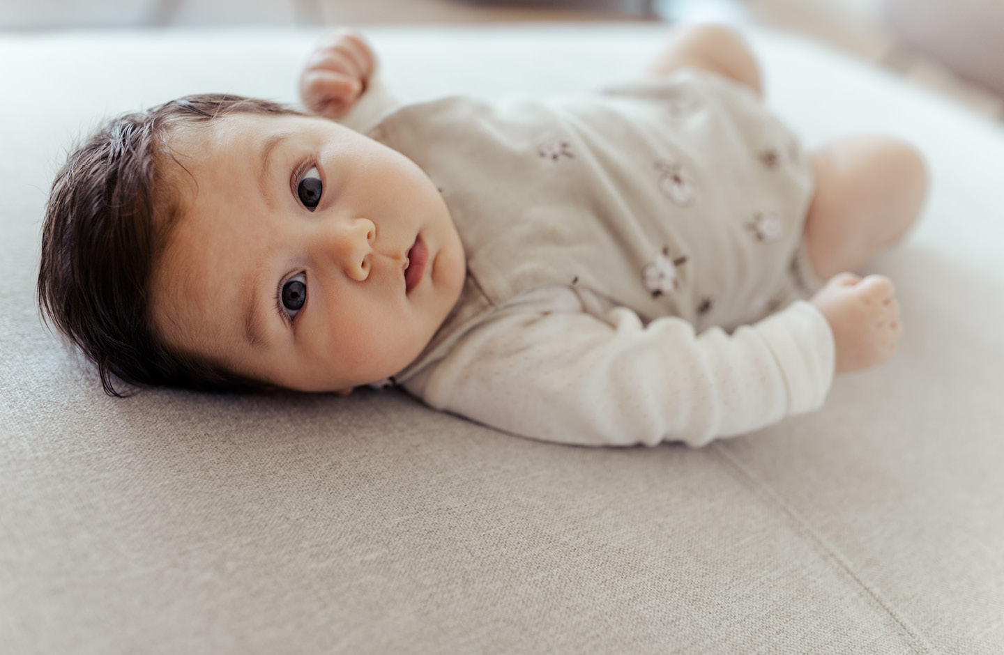 Baby mit dunklen Haaren auf einem Bett liegend