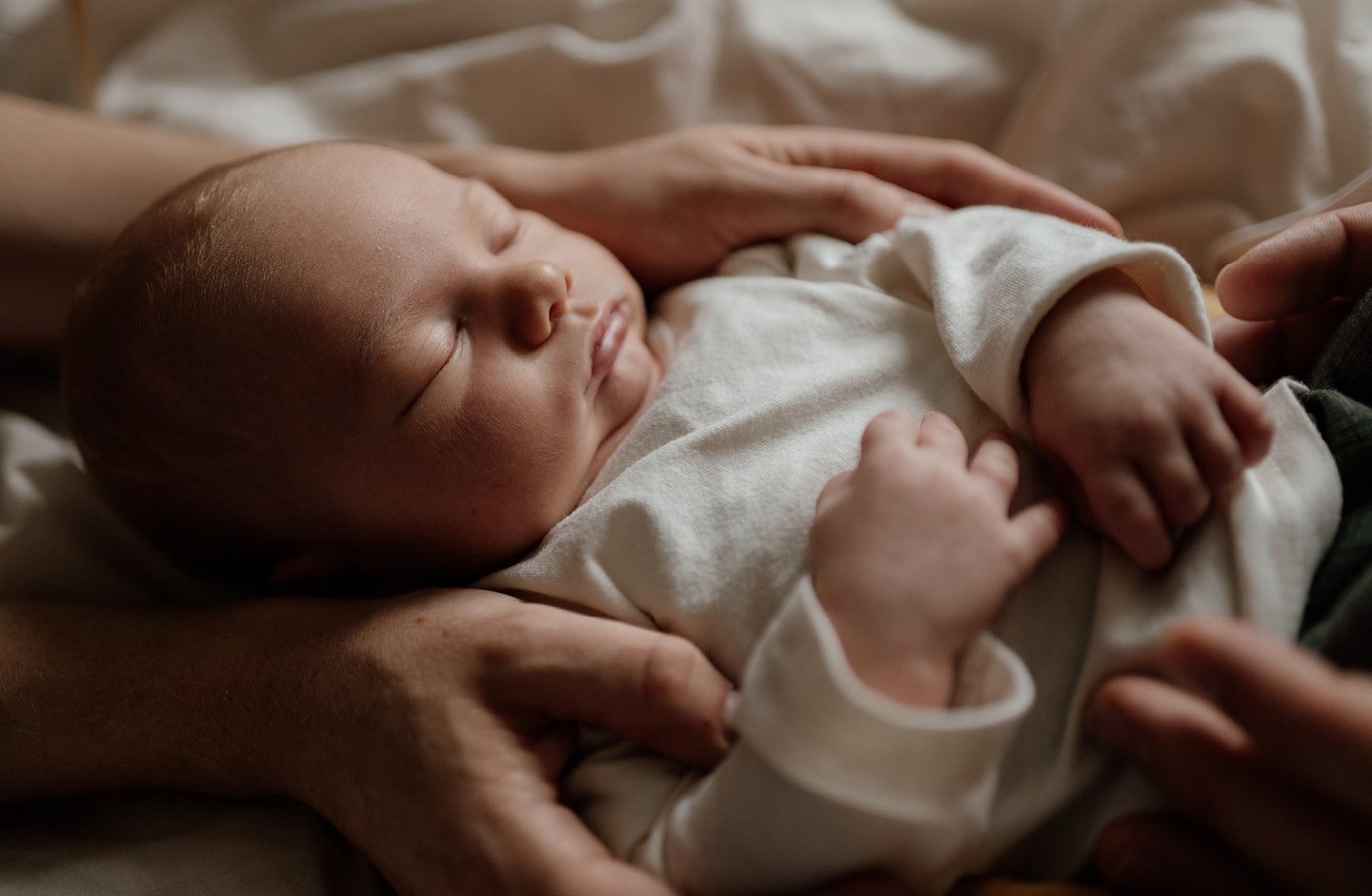 Eltern im Wochenbett umfassen liebevoll schlafendes Baby mit ihren Händen
