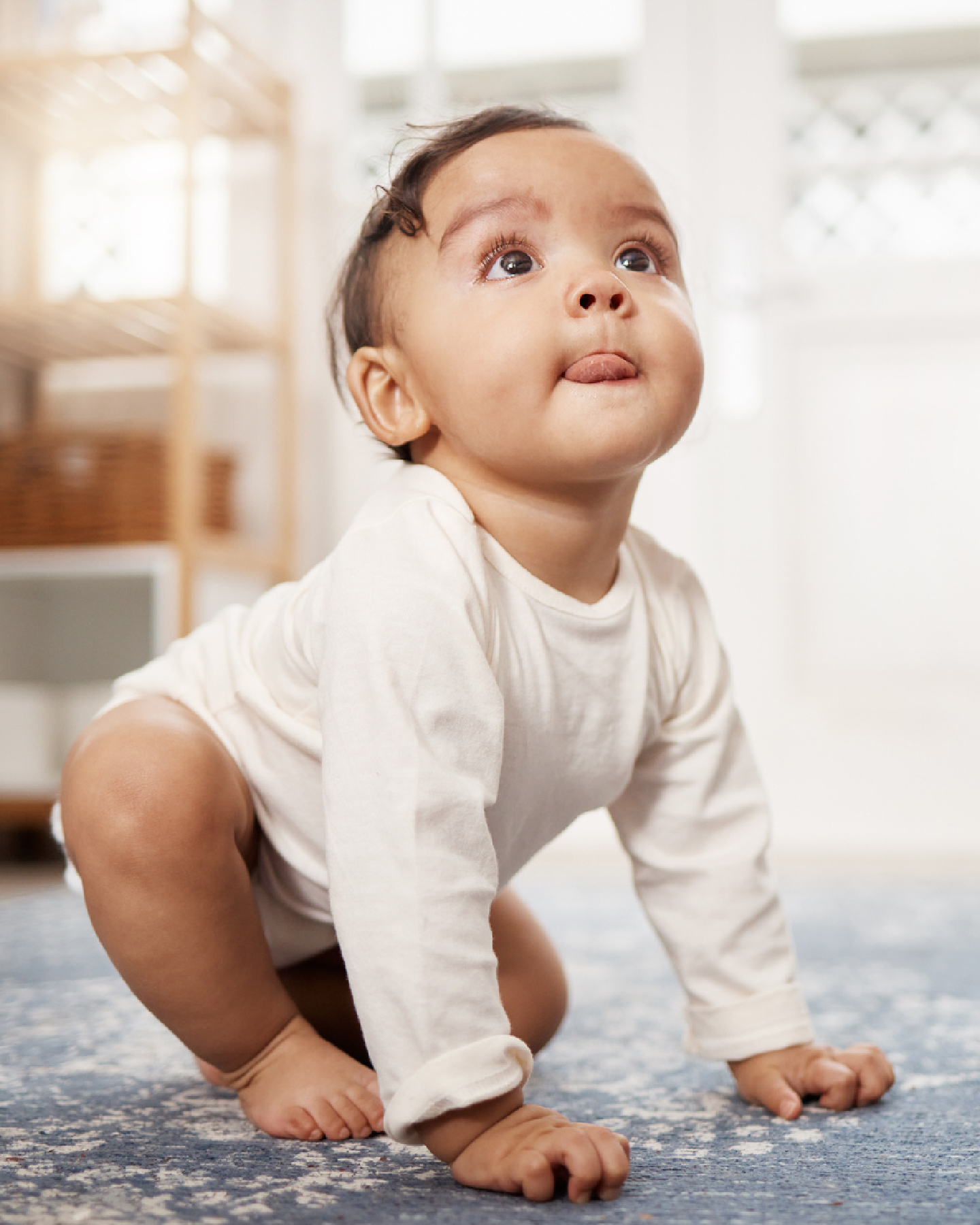 Baby in weißem Body krabbelt auf dem Teppich 