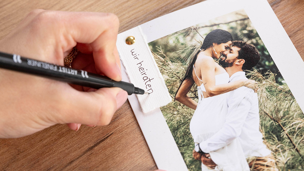DIY-Hochzeitseinladung wird handschriftlich beschriftet. Anhänger mit Schriftzug Wir heiraten