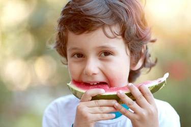 Junge steht im Garten und beißt beherzt in eine Wassermelone.