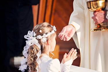 Mädchen kniet vor dem Priester und erhält ihre Erstkommunion durch die Vergabe des Leib Christi