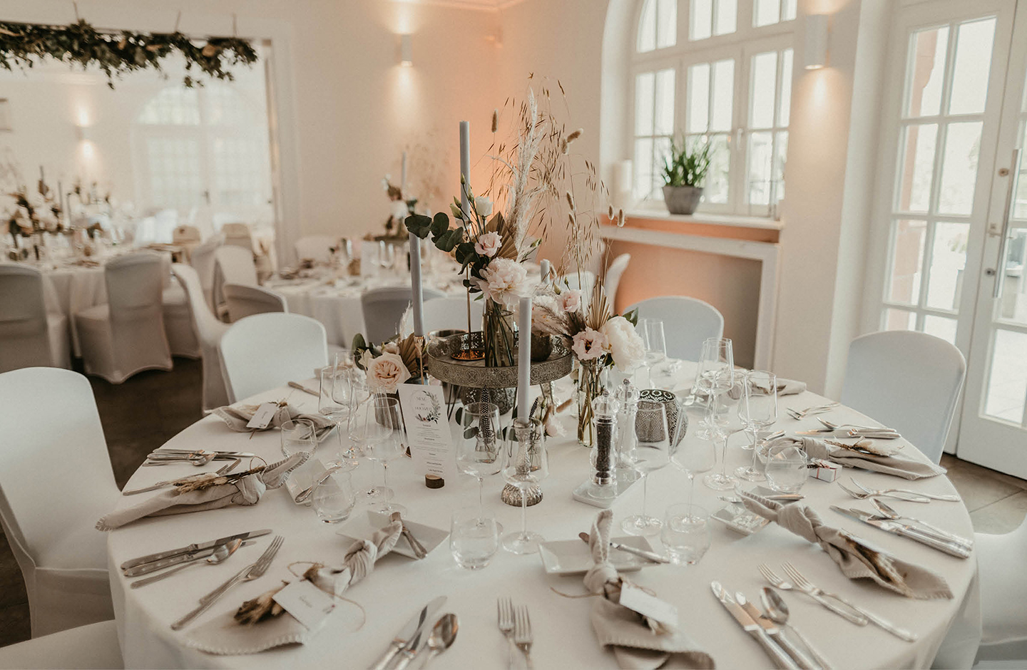 Runde Hochzeitstafel, festlich gedeckt mit weiß und beigefarbener Dekoration.