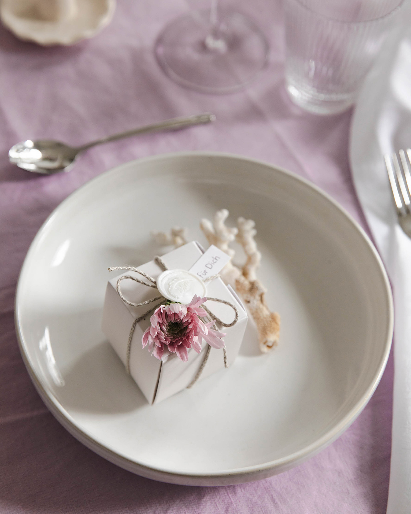 Geschenkbox mit Macaron liegt auf dem Teller einer gedeckten Hochzeitstafel. Gastgeschenke Hochzeit selber machen.