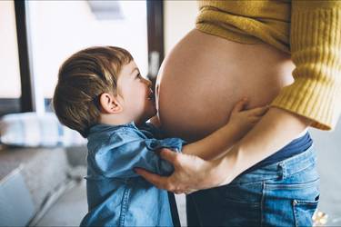 Kleiner JungE umarmt Babybauch seiner Mutter