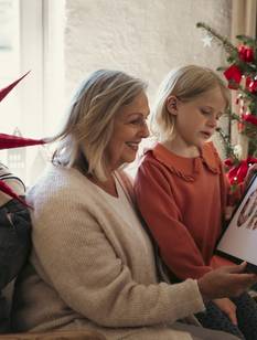 Oma sitzt mit zwei Kindern vor dem Weihnachtsbaum und schaut ein Bild an.