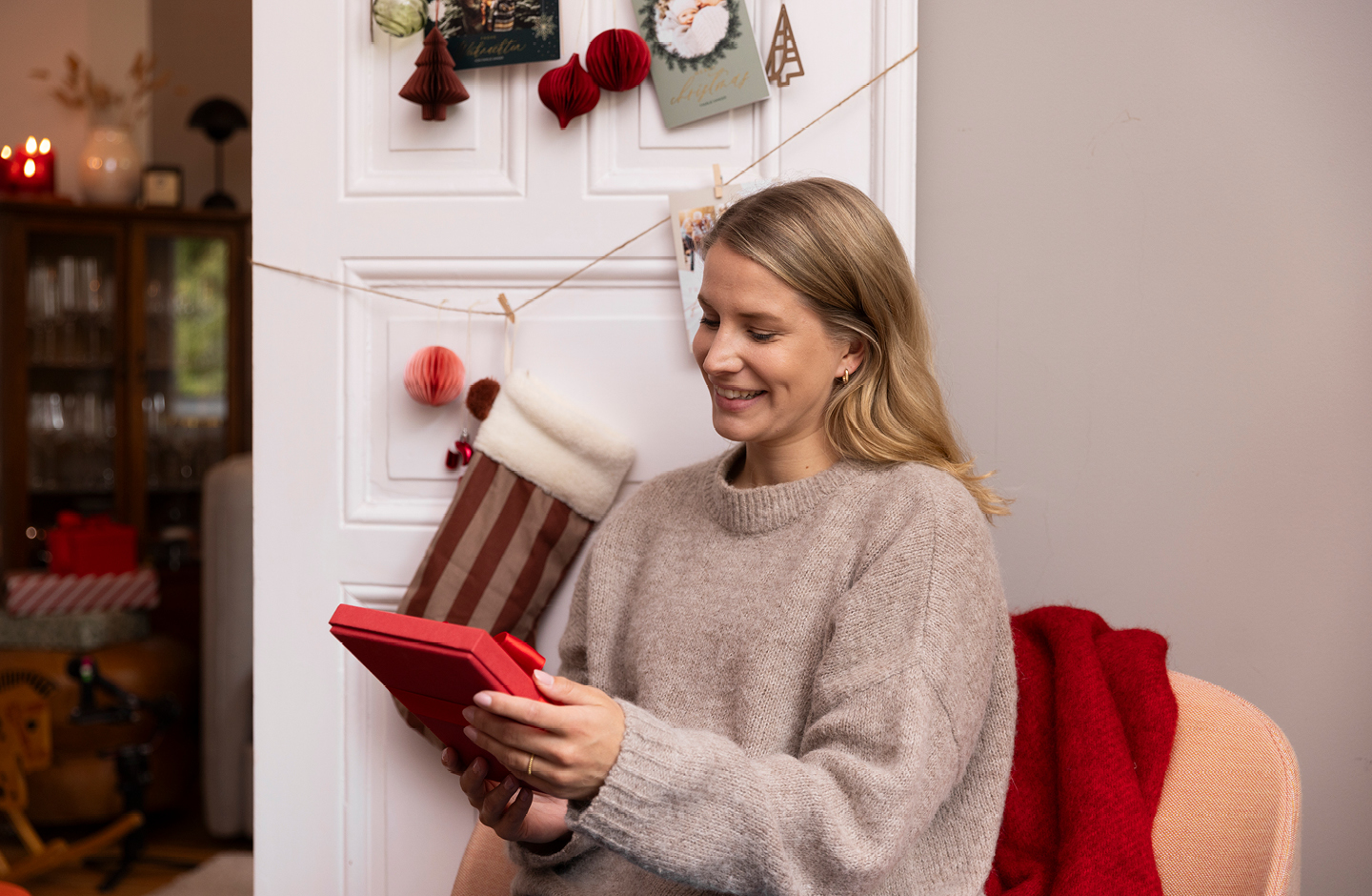 Lächelnde junge Frau mit Geschenk in der Hand, im Sessel vor weihnachtlich geschmückter Tür