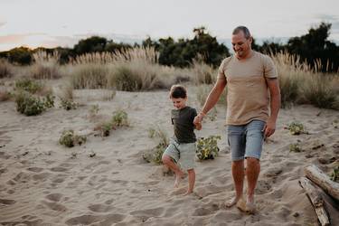 Vater und etwa 8-jähriger Sohn gehen am Vatertag Hand in Hand am Strand spazieren