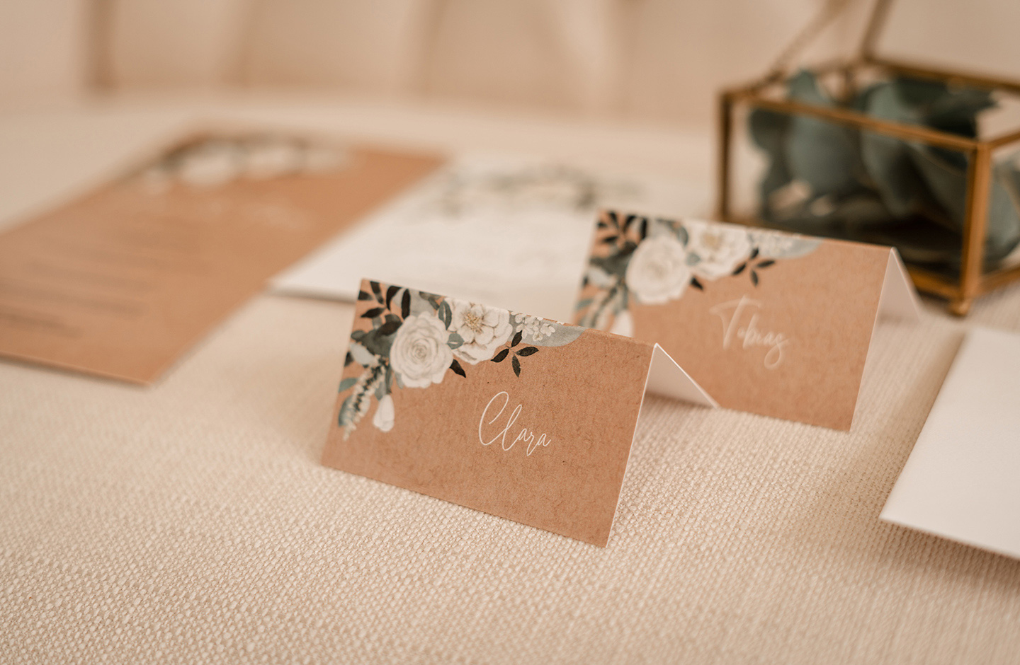 Tischkarten mit weißen Blüten und grünen Blättern auf. Kraftpapierhintergrund