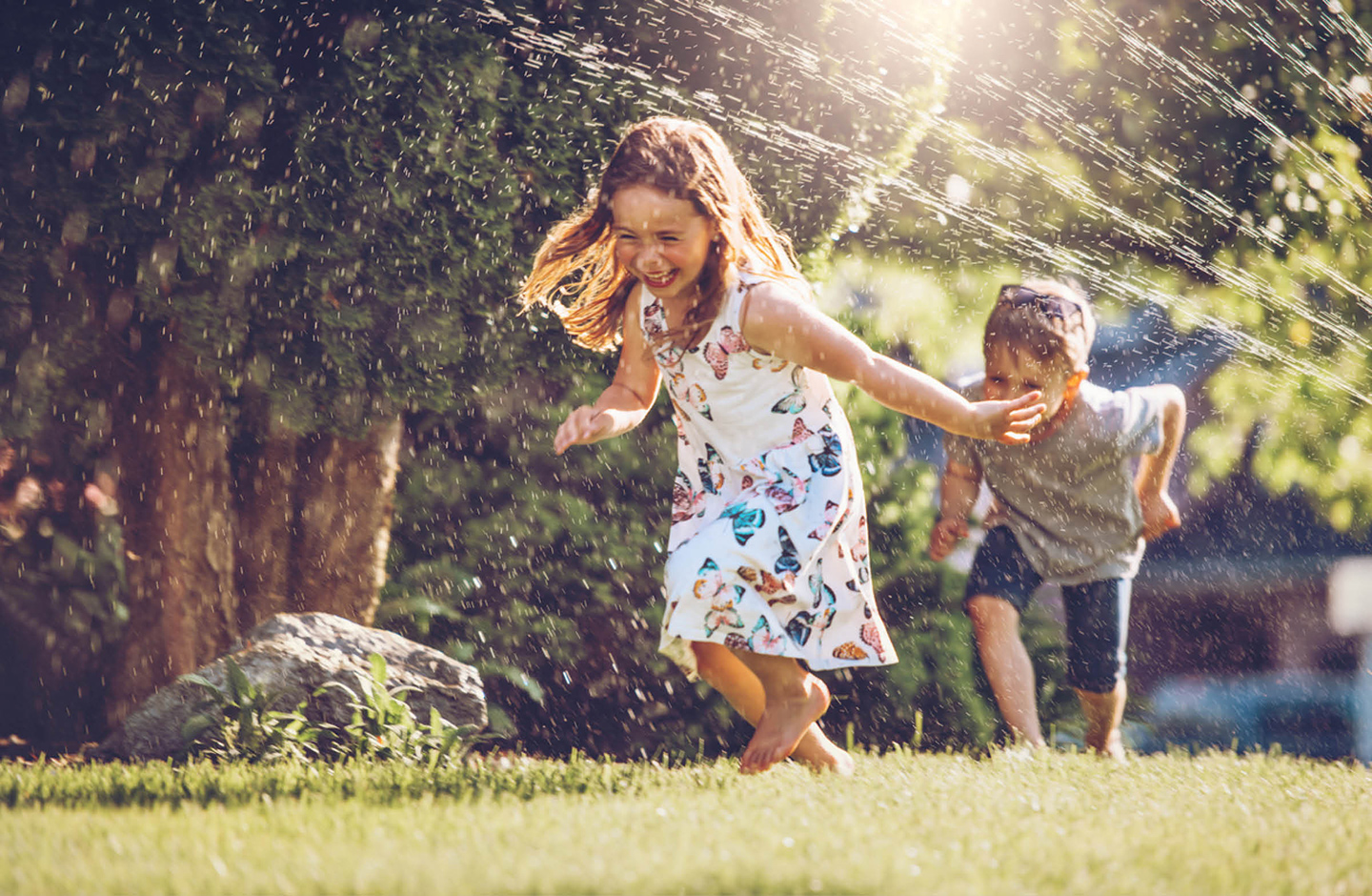 Kinder laufen im Garten unterm Rasensprenger durch