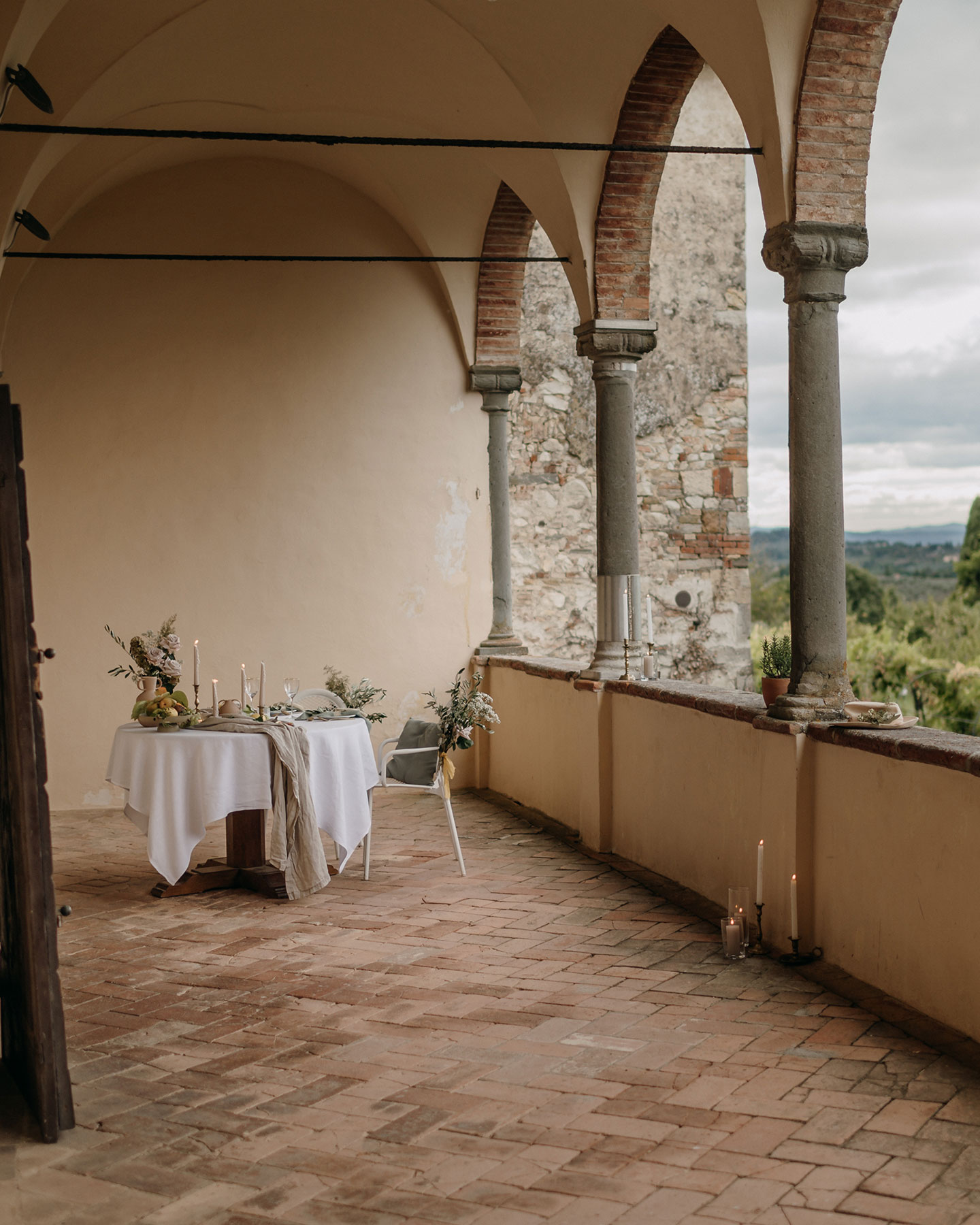 Der gedeckte Hochzeitstisch befindet sich im überdachten Balkonbereich der Hochzeitslocation in Italien. Er ist geschmückt mit einer weißen Tischdeko, Blumenarrangements und Kerzen, sowie Zitrusfrüchten und Feigen.