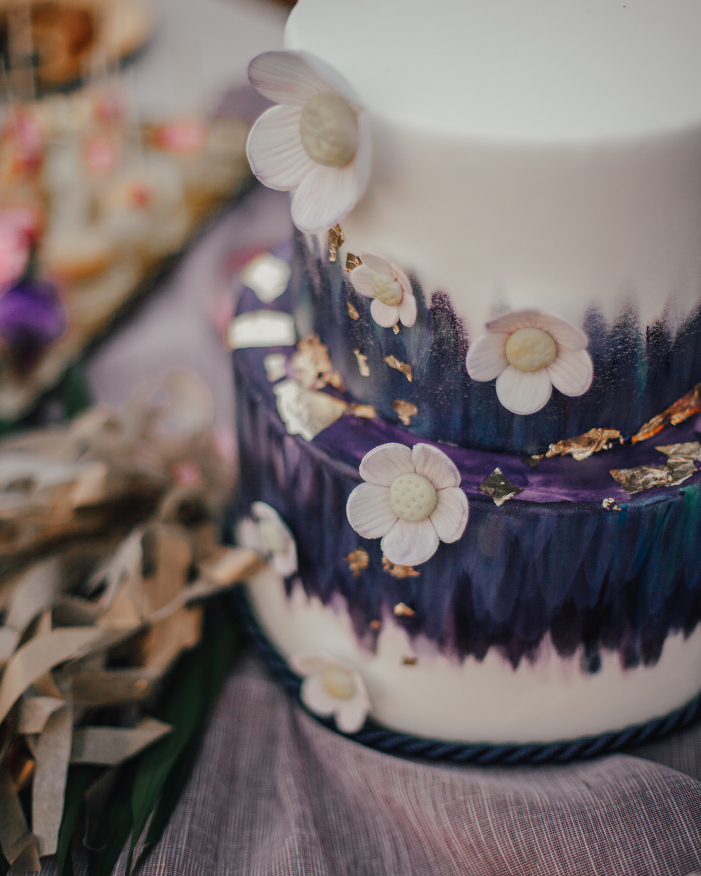 Kunstvoll verzierte Hochzeitstorte in Weiß und Violett mit Zuckerblüten und Blattgold