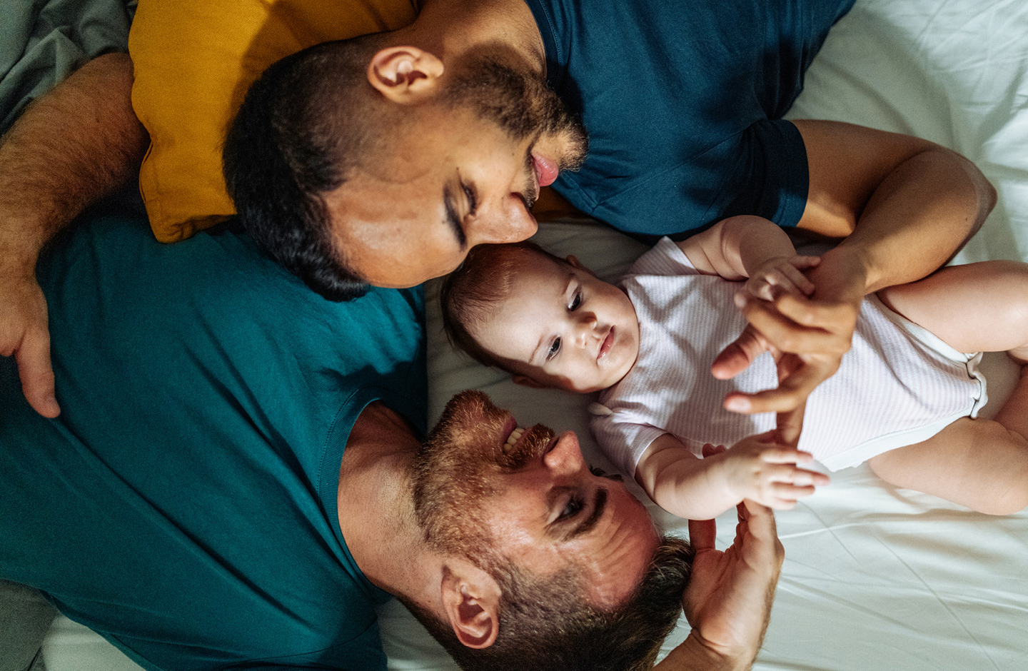 Zwei Papas kuscheln mit ihrem Baby auf dem Bett