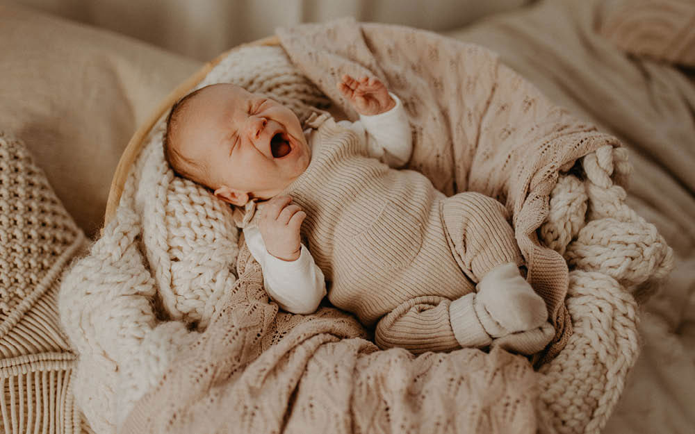 Schlafendes Baby liegt in einem kuscheligen Körbchen und gähnt