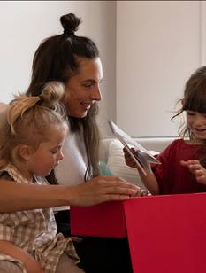 Frau auf der Couch mit 2 kleinen Mädchen öffnet ihr Weihnachtsgeschenk