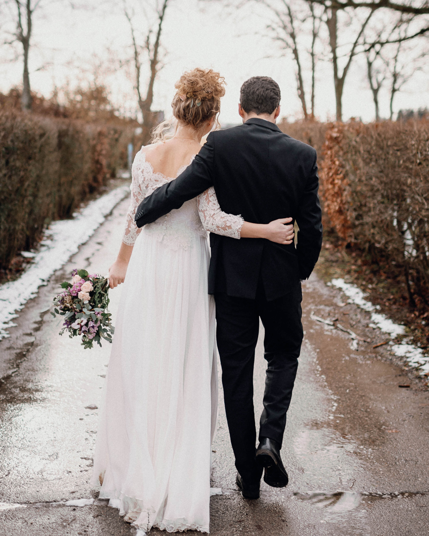 Brautpaar geht Arm in Arm einen Weg entlang