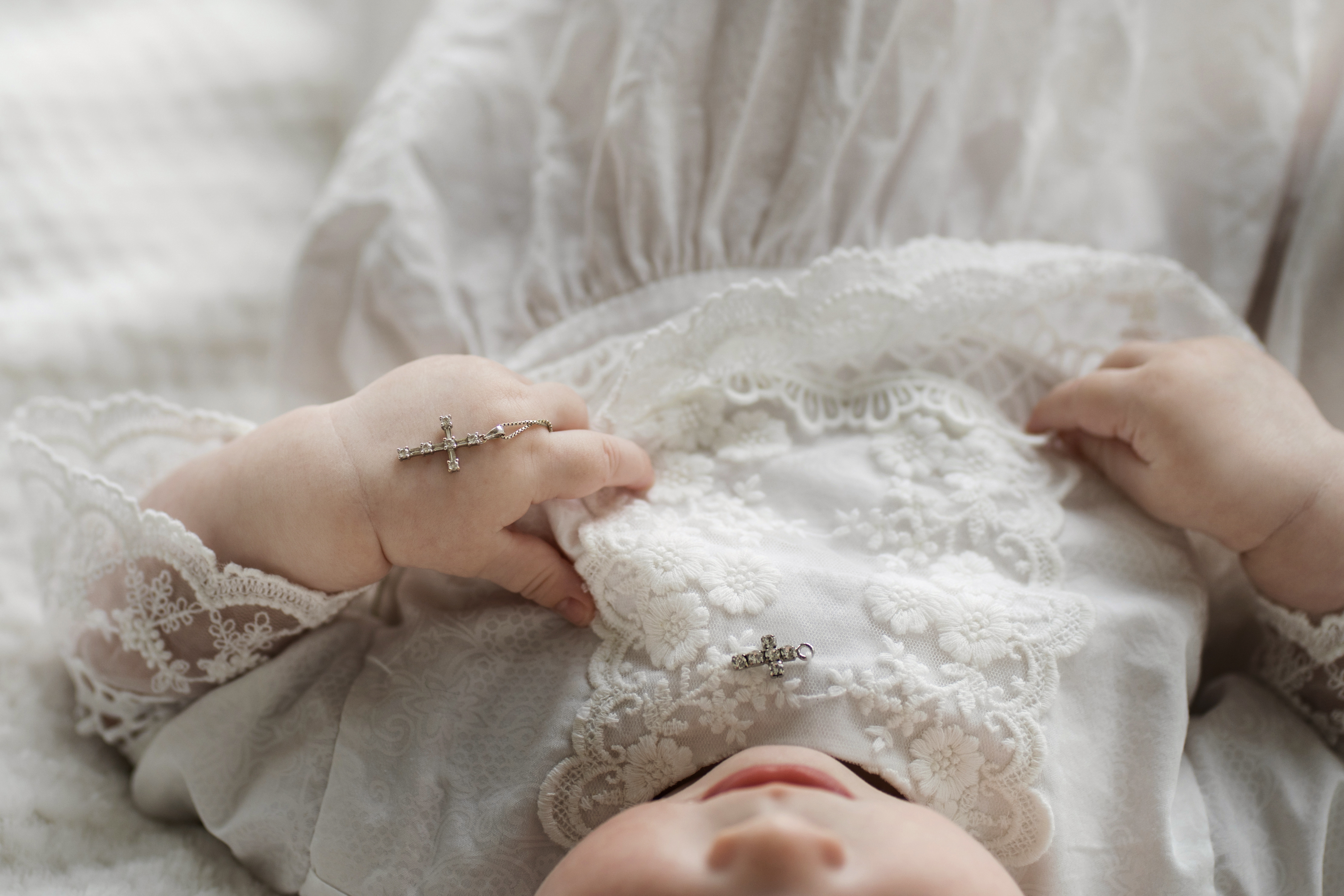 Baby in weißem Kleid hält Kreuz