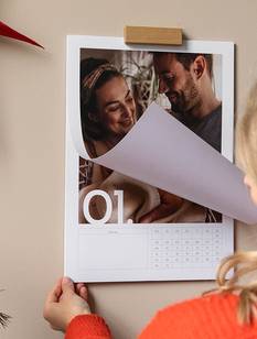 Fotokalender hängt an der Wand. Frau blättert die erste Seite des Kalenders um.