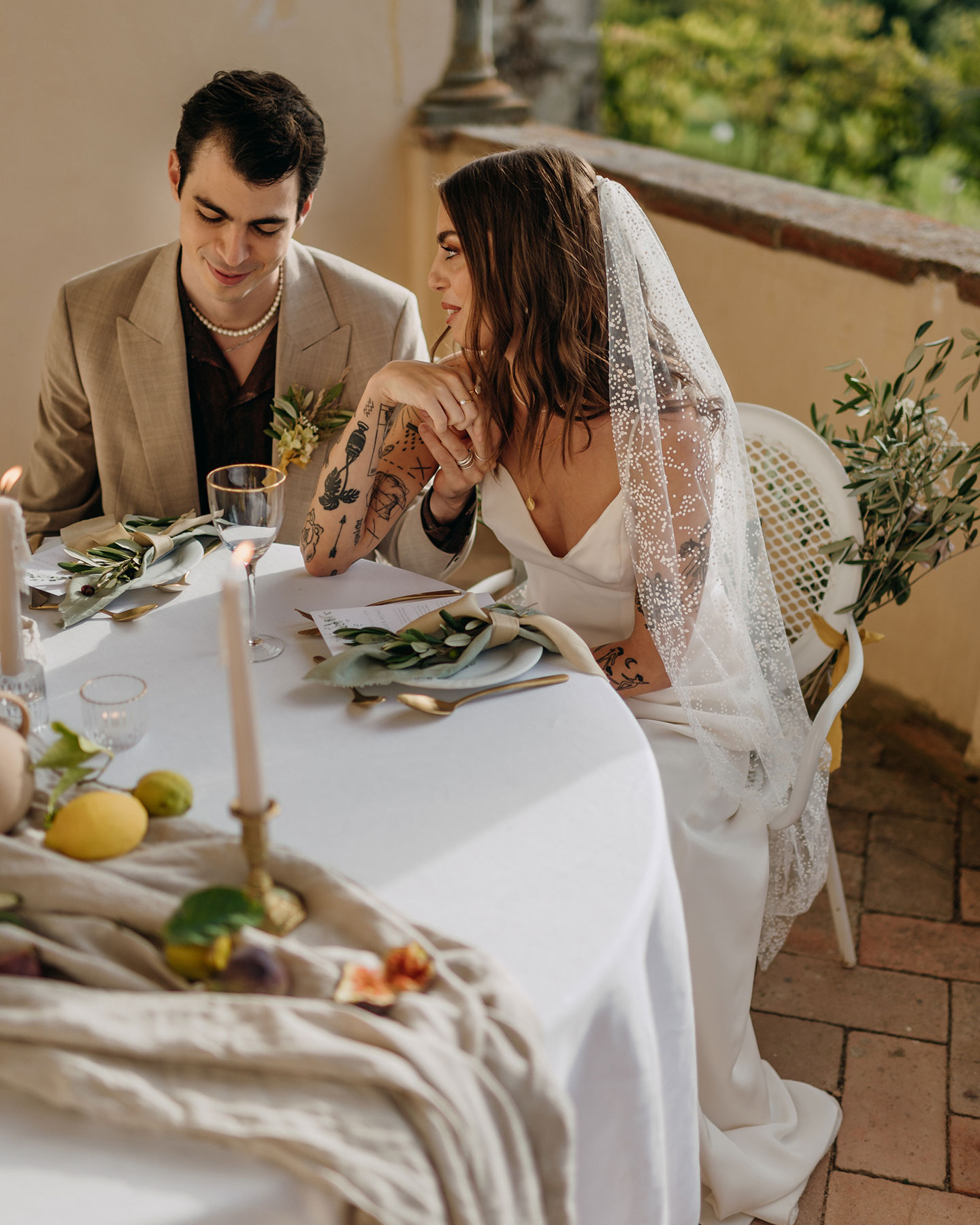Das Hochzeitspaar sitzt am gedeckten Hochzeitstisch und die Braut schaut den Bräutigam verliebt an.