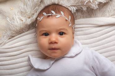 Baby in Weiß gekleidet mit weißer Ranke als Kopfschmuck