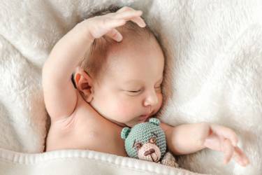Auf einer Decke schlafendes Baby mit kleinem gehäkelten Bären im Arm