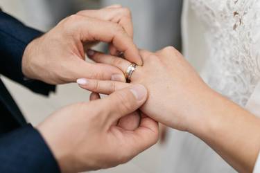 Mann steckt bei der Hochzeit seiner Frau den Ring an den Finger, Bildausschnitt der Hände