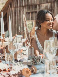 Hochzeitspaar im Vintage Boho Look küsst sich an der Hochzeitstafel.