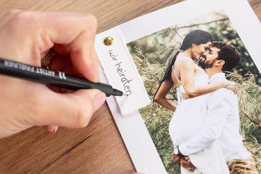 DIY-Hochzeitseinladung wird handschriftlich beschriftet. Anhänger mit Schriftzug Wir heiraten