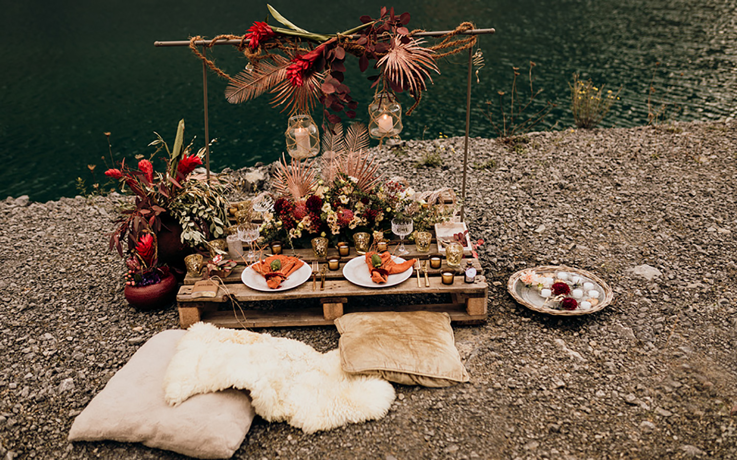 Tischdeko Hochzeit: Boho-Look im Steinbruch: Der Hochzeitstisch aus einer Holzpalette ist liebevoll geschmückt in warmen, leuchtenden Farben. Rot, Orange und Beige wirken wunderbar zusammen kombiniert.