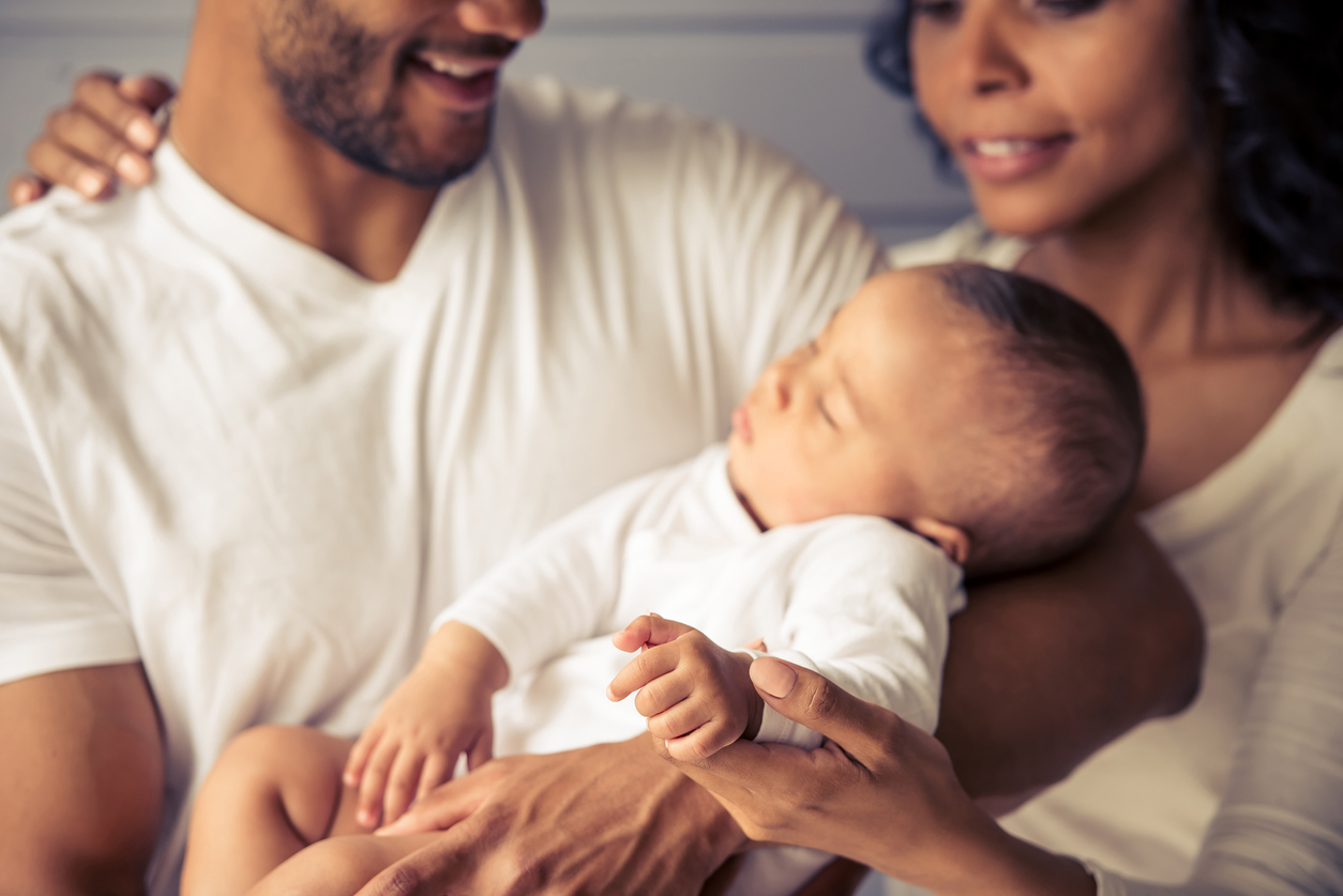 Junge Mutter umarmt jungen Papa mit Baby auf dem Arm