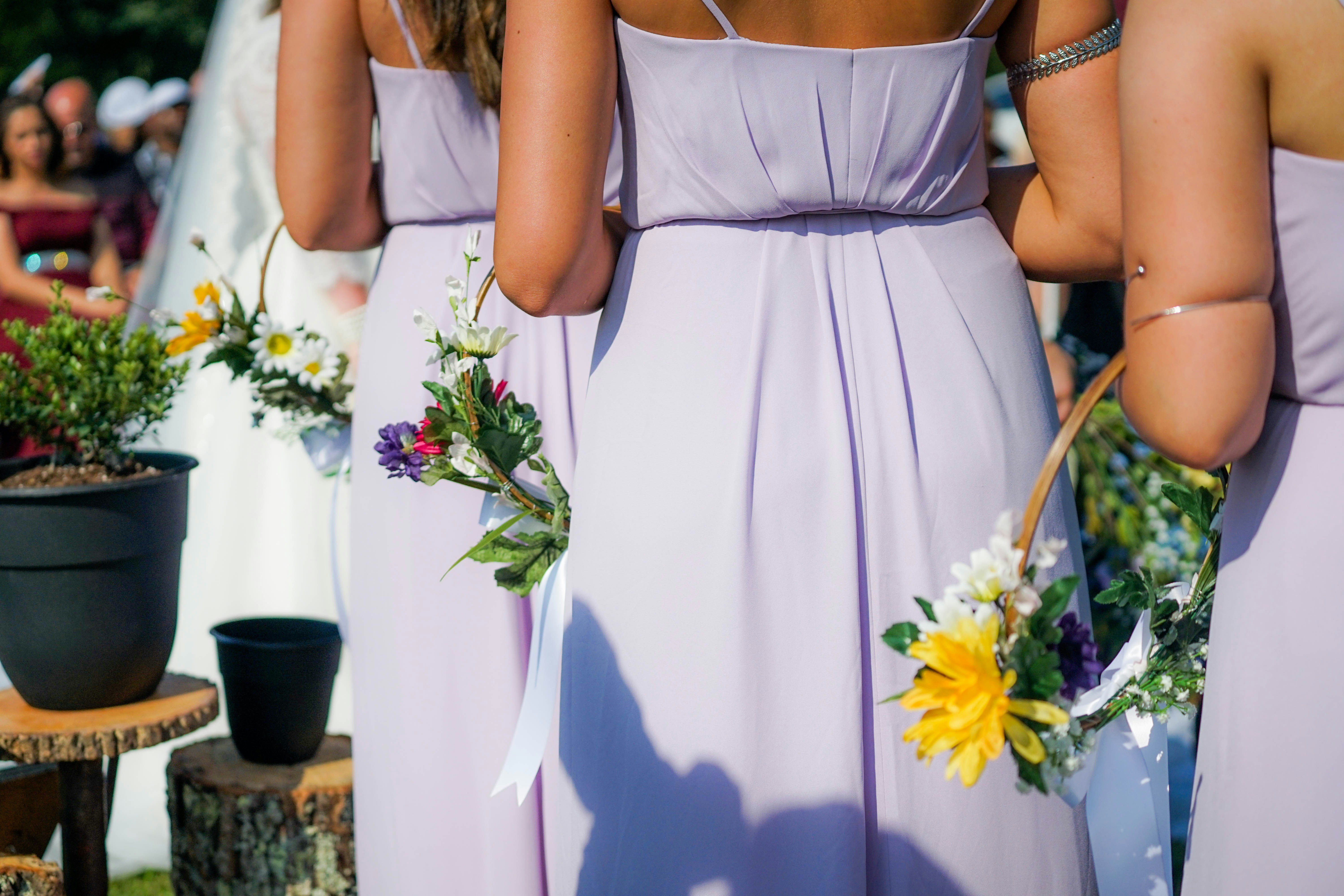 weibliche Hochzeitsgäste in violetten Kleidern mit Blumengestecke von hinten