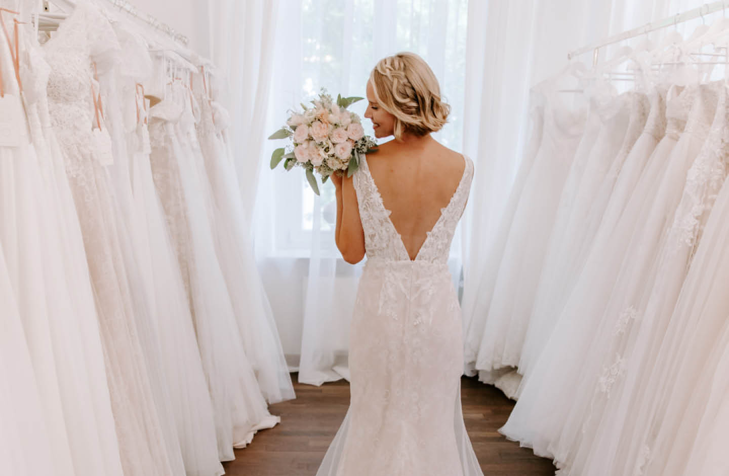 Frau mit Hochzeitskleid steht zwischen mehreren Hochzeitskleidern.