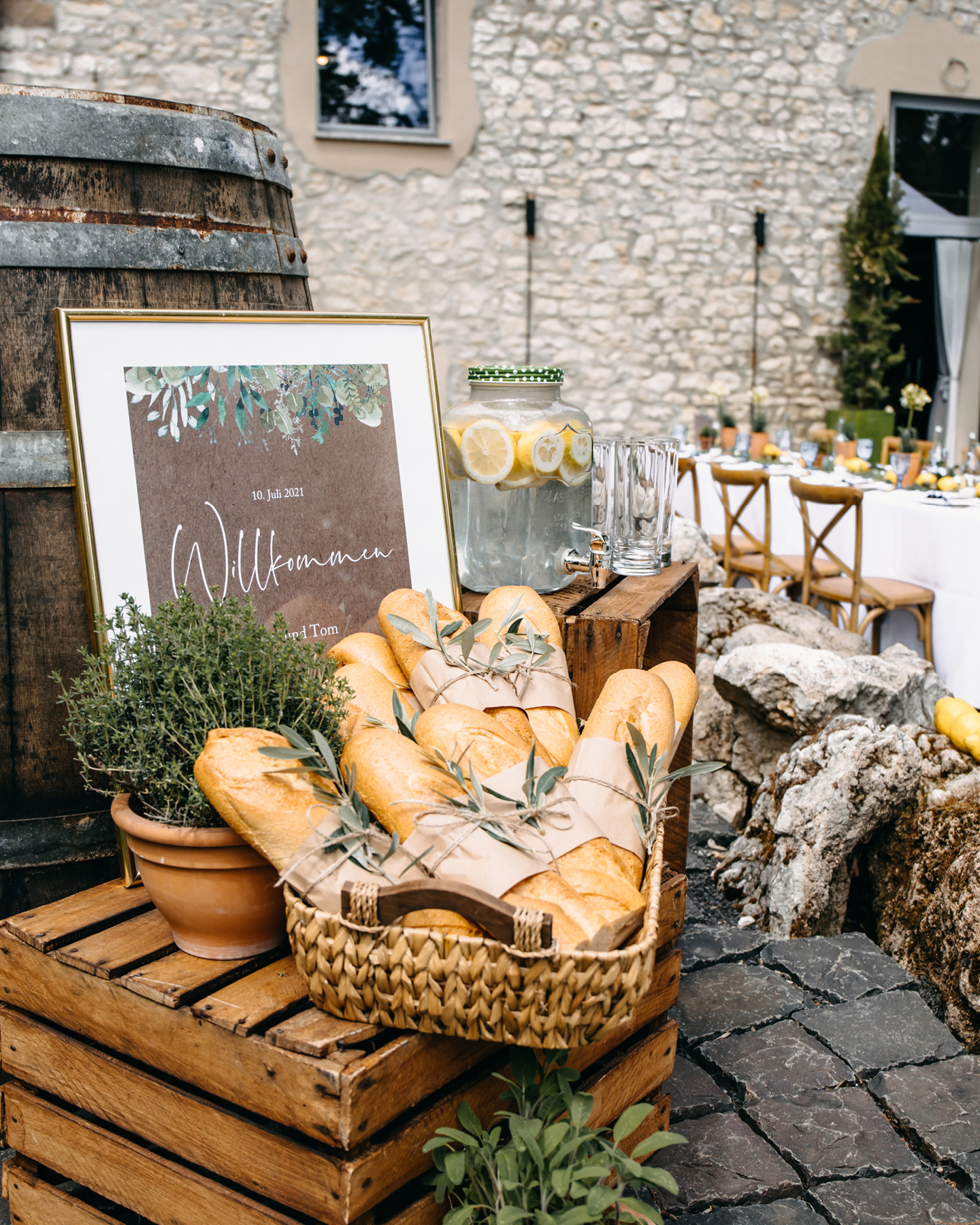 Wilkommensschild aus Kraftpapier begrüßt Gäste zur Feier am Weingut, wo geheiratet wird. Baguette liegt im Korb und Zitronenlimonade steht bereit.