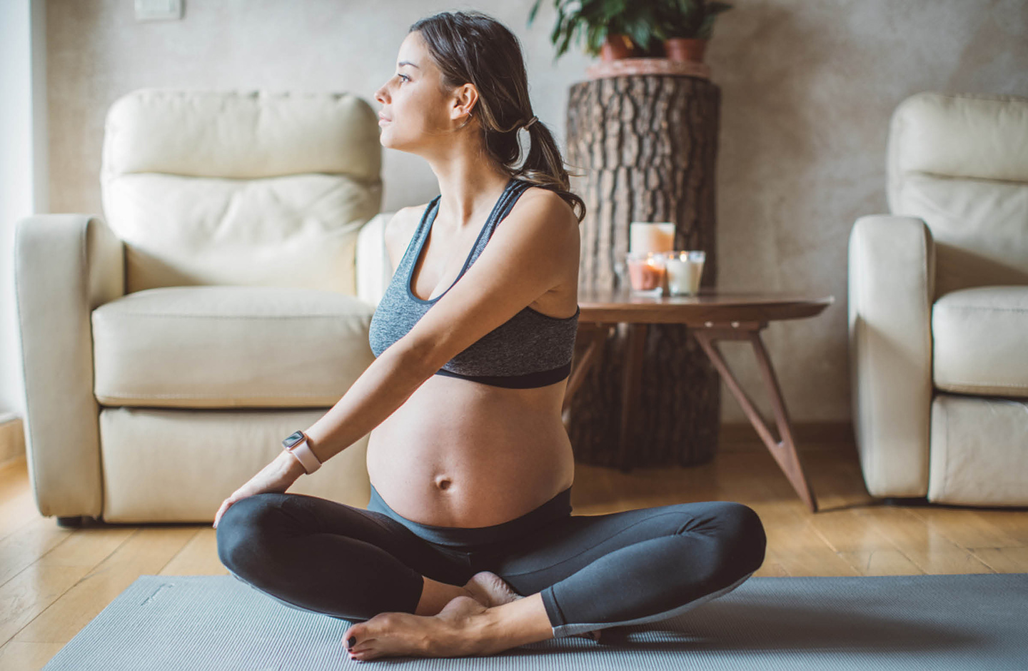 Schwangere macht Yogaübungen in ihrem Wohnzimmer.