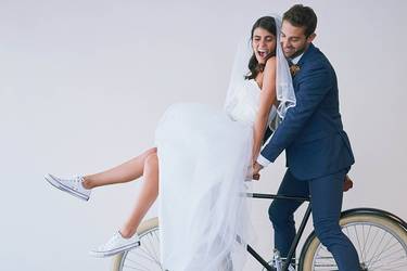 Frisch vermähltes Hochzeitspaar fährt zusammen auf einem Fahrrad. Die Frau trägt Chucks.