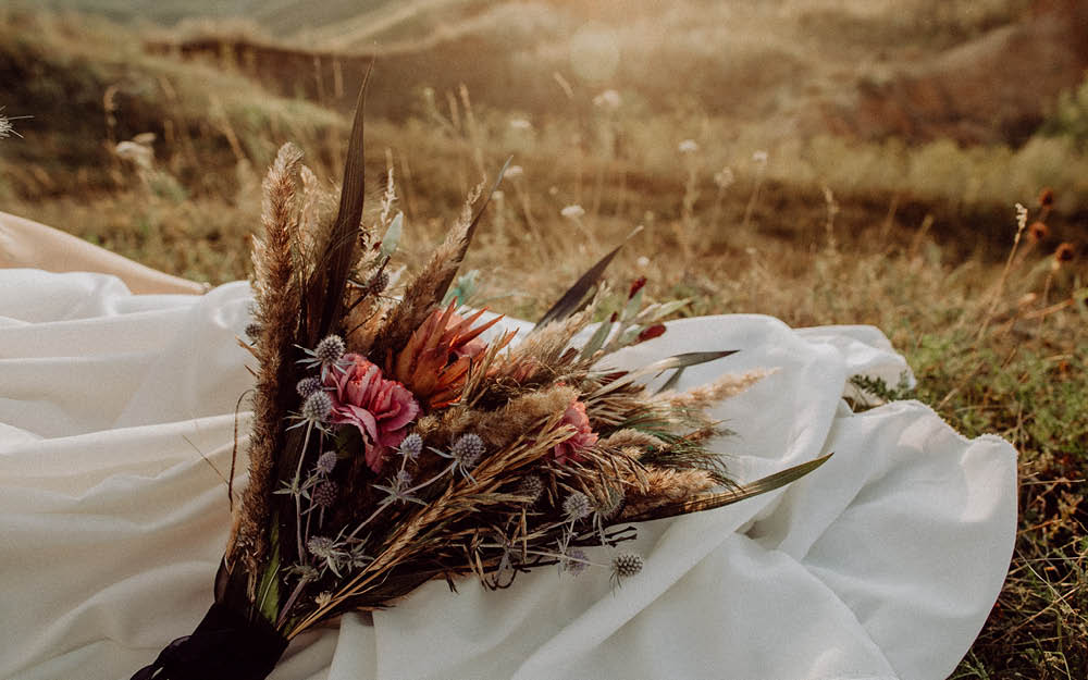Brautstrauß mit Trockenblumen und Diesteln liegt auf weißem Schleier