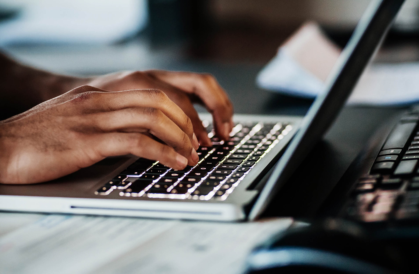 Nahaufnahme von zwei Händen, die auf der Tastatur eines Laptops tippen.
