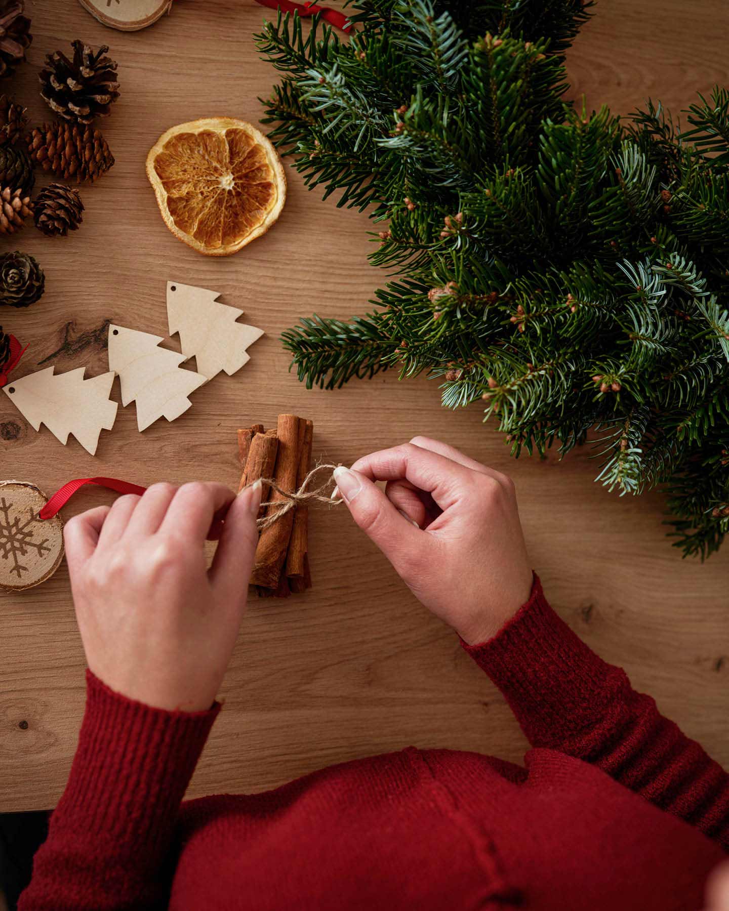 Frau bindet Zimstangen zu selbstgemachten Weihnachtsbaumschmuck zusammen.