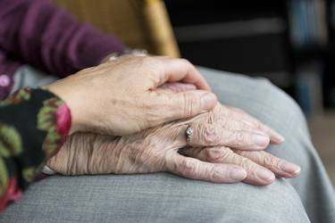 Hände von älteren Menschen halten sich mit Diamantring am Finger