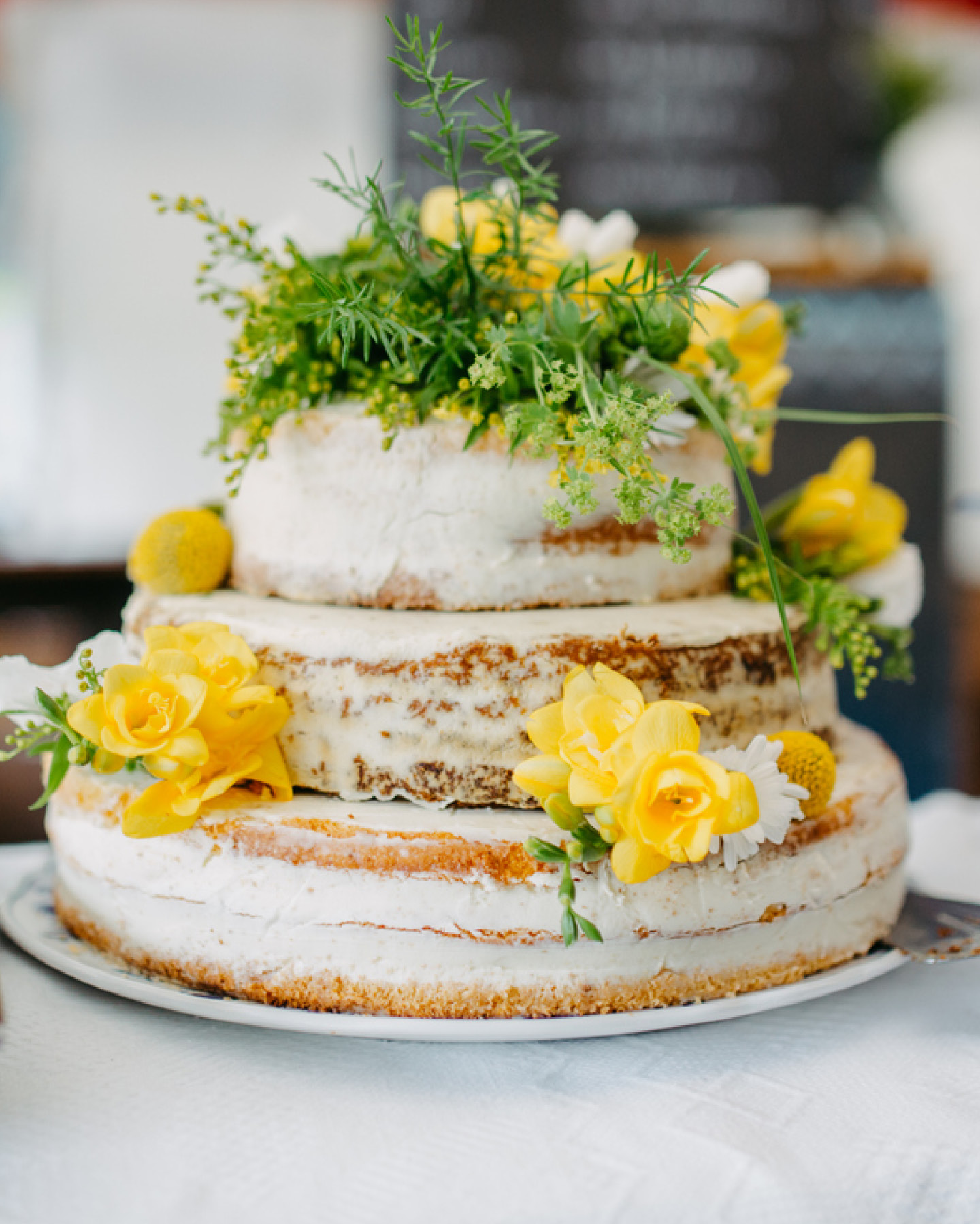 Sommerliche Hochzeitstorte mit gelben Blüten und Kräutern verziert