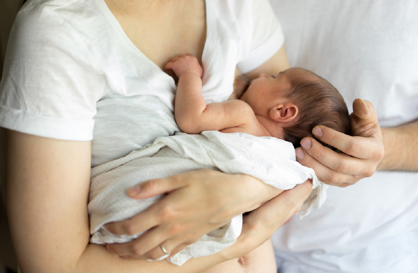 Baby saugt an der Brust der Mutter, der Vater hält das Köpfchen