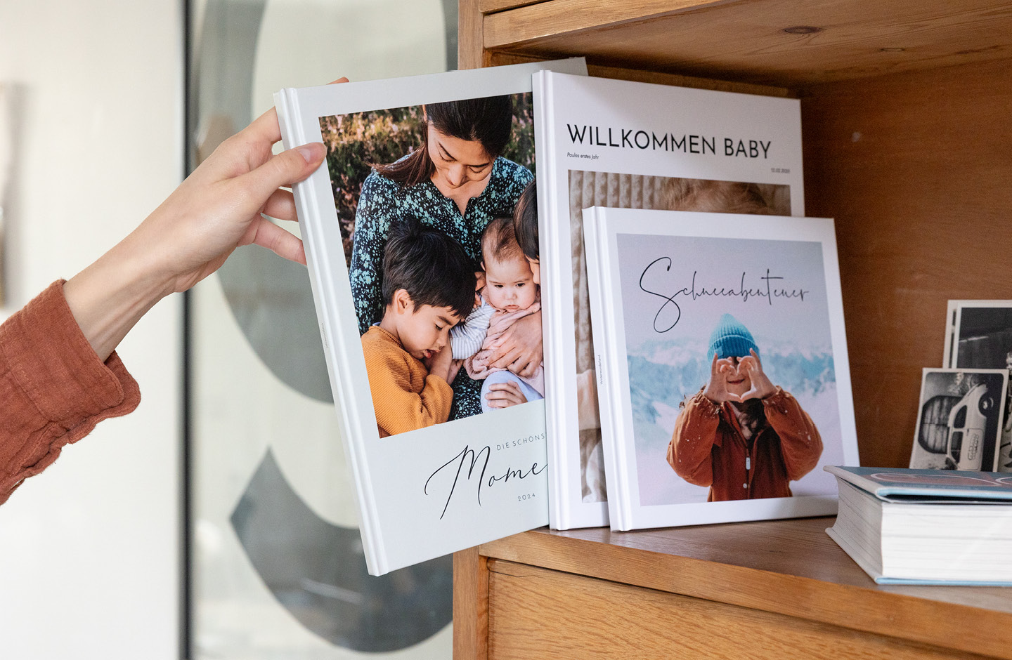 Drei dekorative Fotobücher in verschiedenen Ausführungen in einem hellen Holzregal