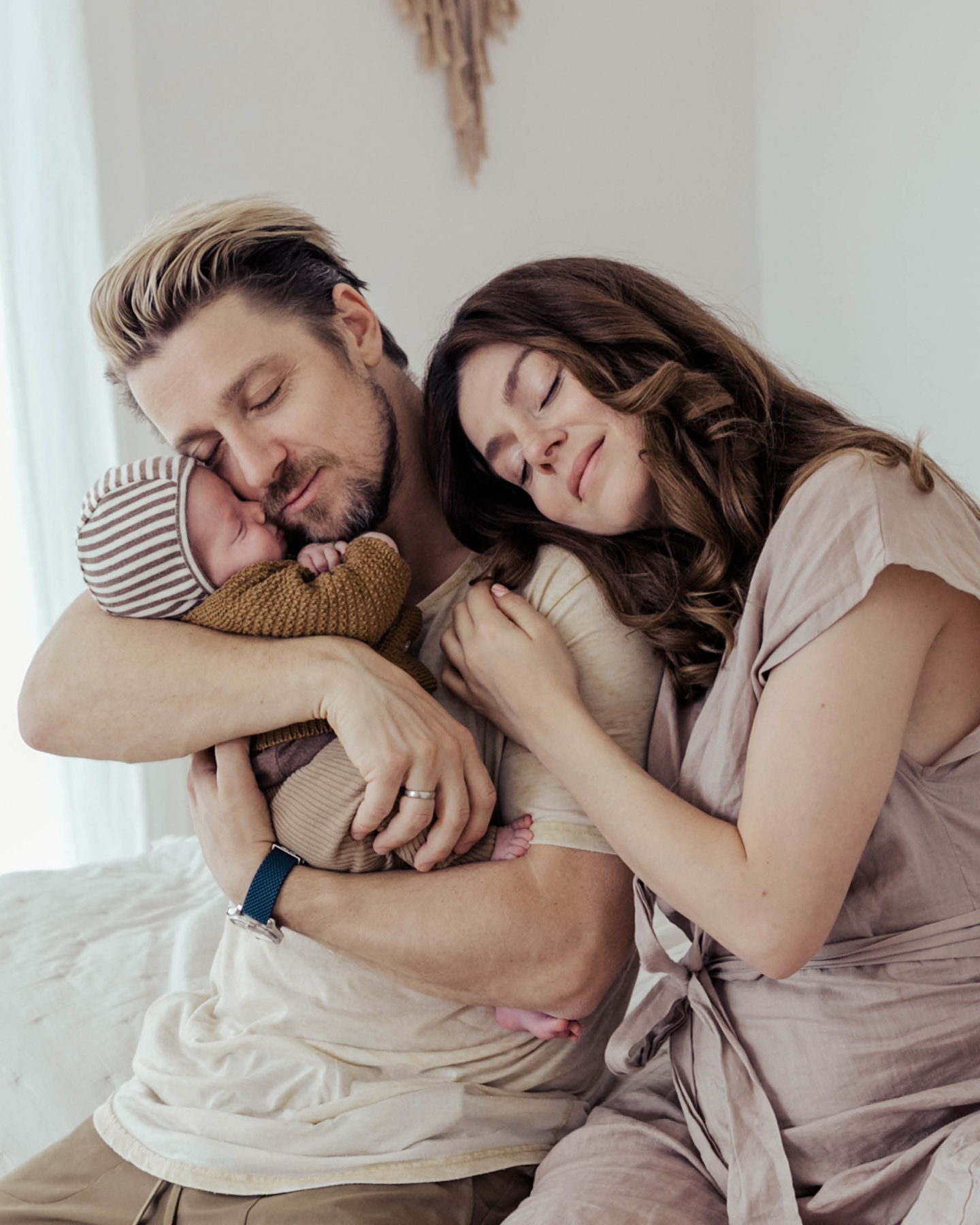 Frisch gebackene Eltern sitzen gemeinsam auf dem Bett und kuscheln mit ihrem Neugeborenen.