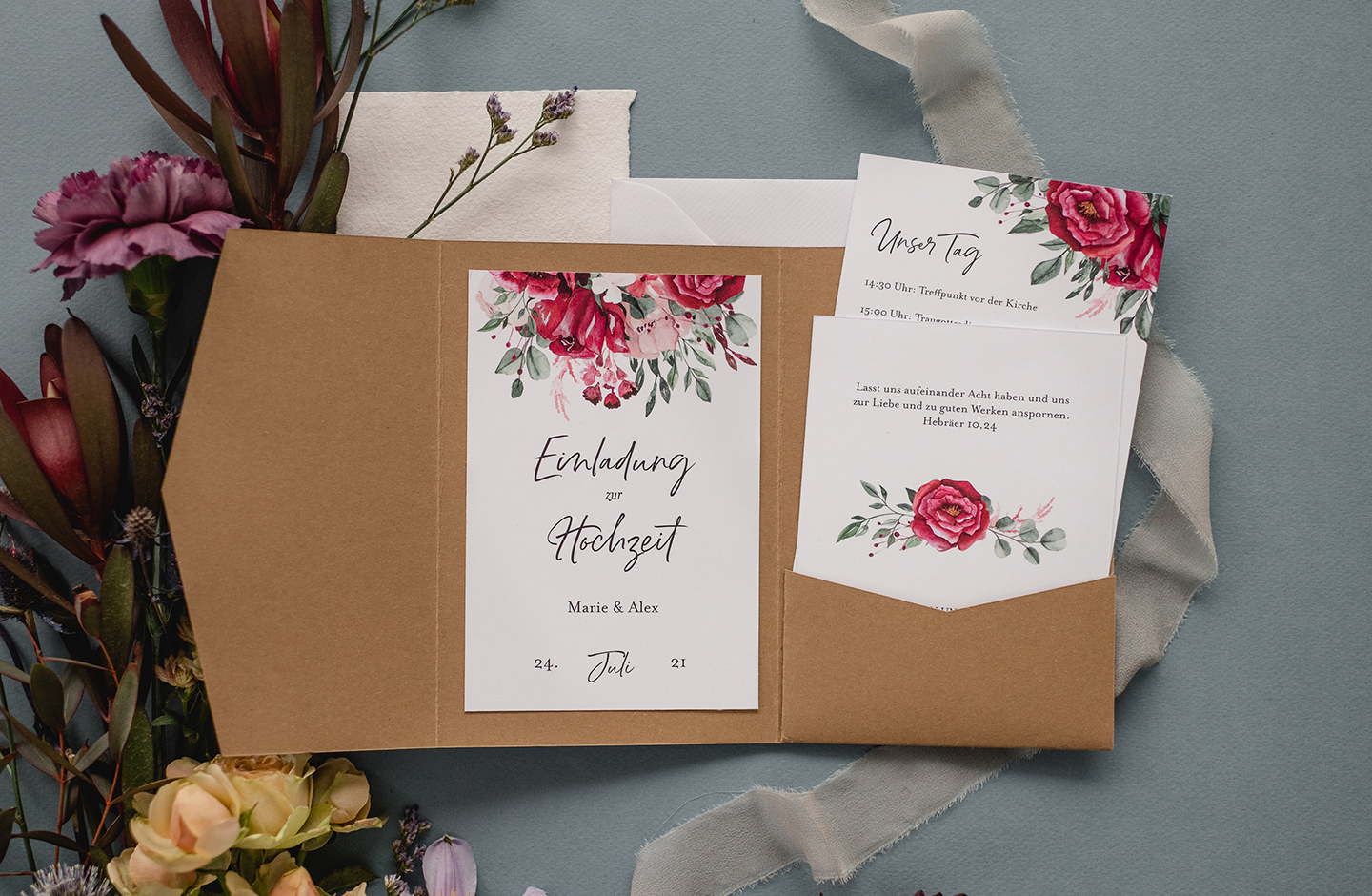 Hochzeitstrend 2021: Pocketfold Einladung aus Kraftpapier mit floralem Design liegt auf hellblauem Hintergrund.