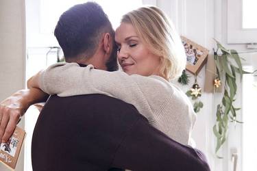 Verliebtes Paar umarmt sich vor weihnachtlich geschmücktem Fenster