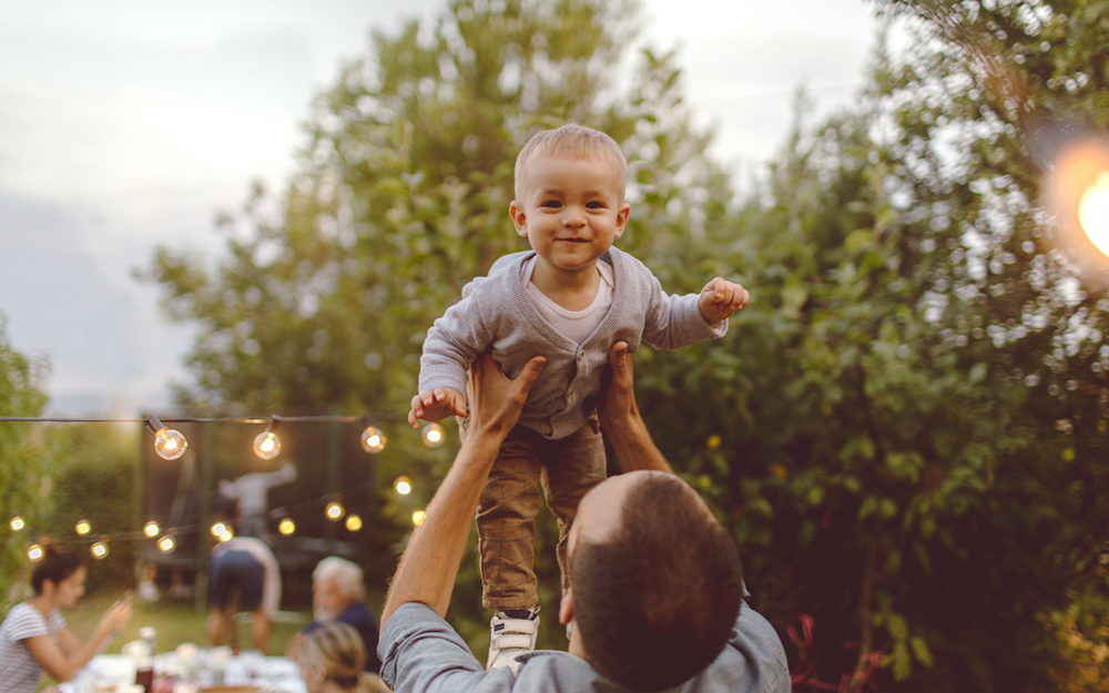 Vater hebt seinen Sohn bei Taufe im Garten hoch