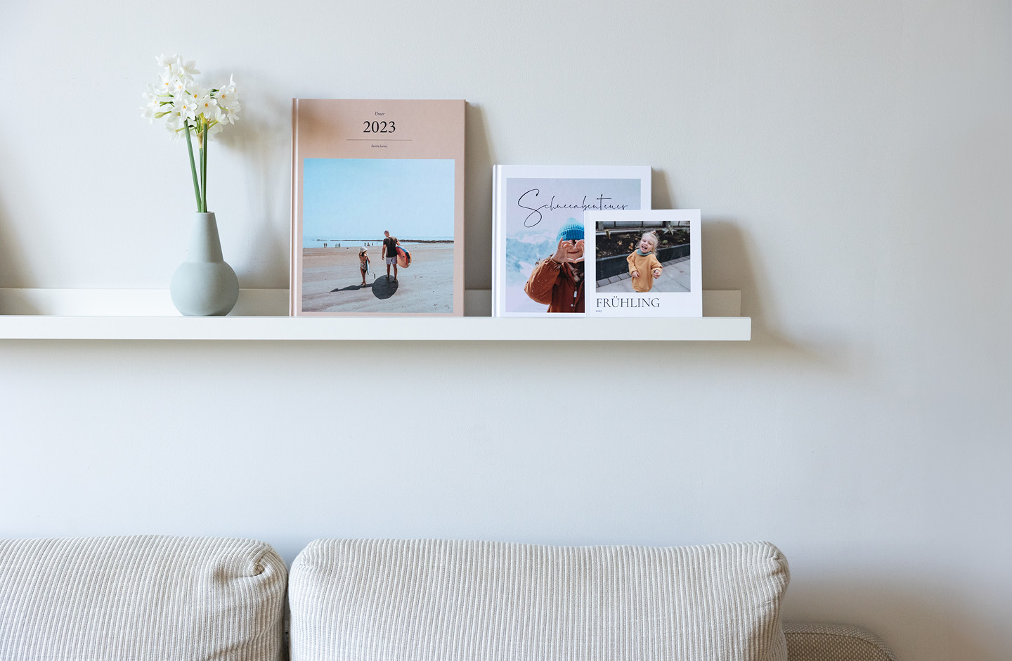 Fotobücher mit den schönsten Moment einer Familie stehen auf einem weißen minimalistischem Regal mit kleiner Blumenvase