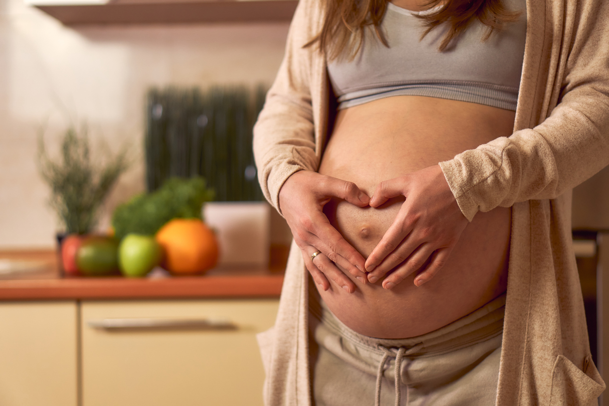 Schwangere legt zärtlich ihre Hände in Herzform auf ihren Bauch