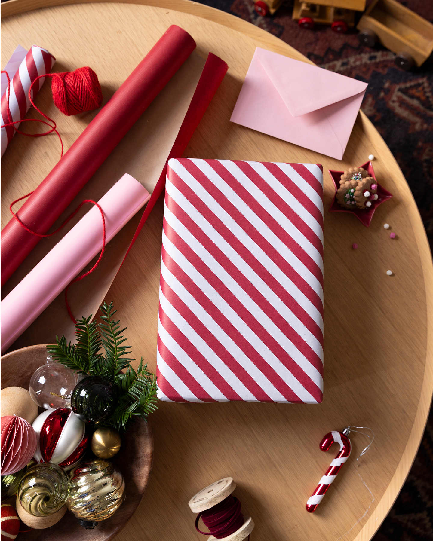 Geschenkpapierrollen, Weihnachtsschmuck und in rotweißem Geschenkpapier eingewickeltes Geschenk auf Holztablett