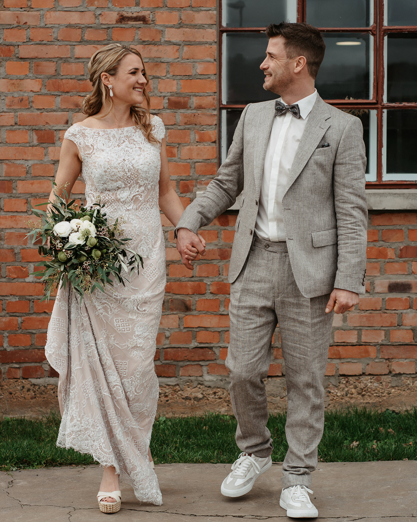 Die Braut in einem creme weißen Hochzeitskleid aus Spitze und der Bräutigam gekleidet in einem grauen Anzug schauen sich verliebt an.